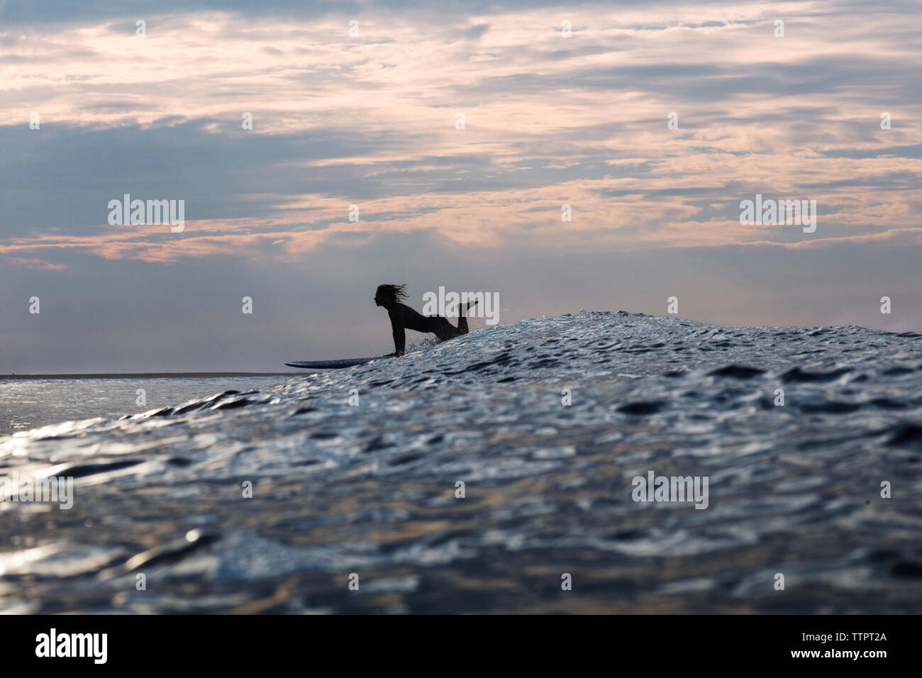 Side view of woman surfboarding on sea during sunset Stock Photo