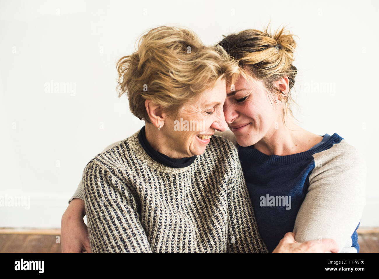 Close-up of smiling mother and daughter sitting against wall at home Stock Photo