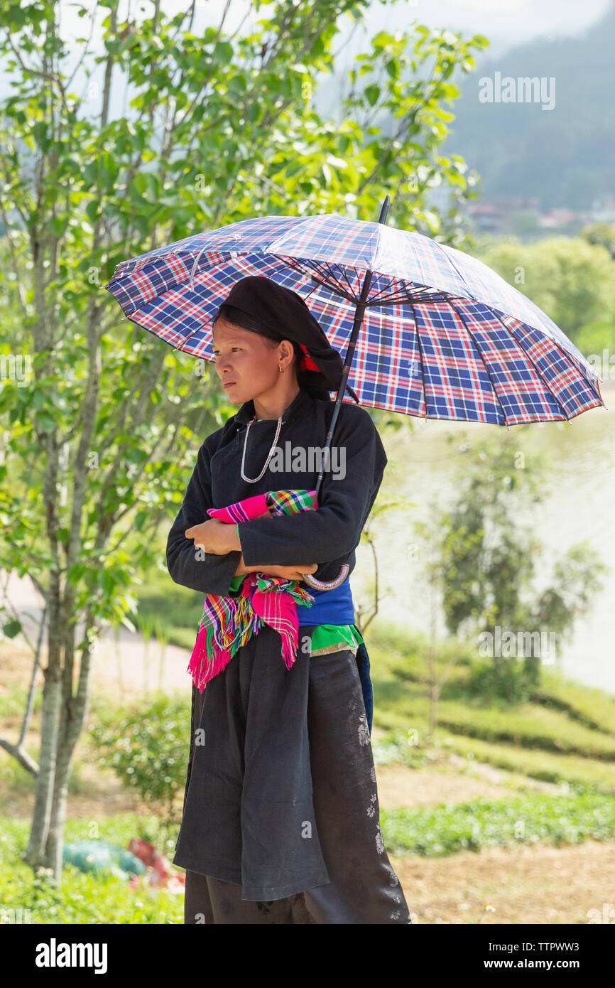 Lone woman standing under umbrella at market, Bac Ha, Lao Cai Province, Vietnam, Asia, Stock Photo