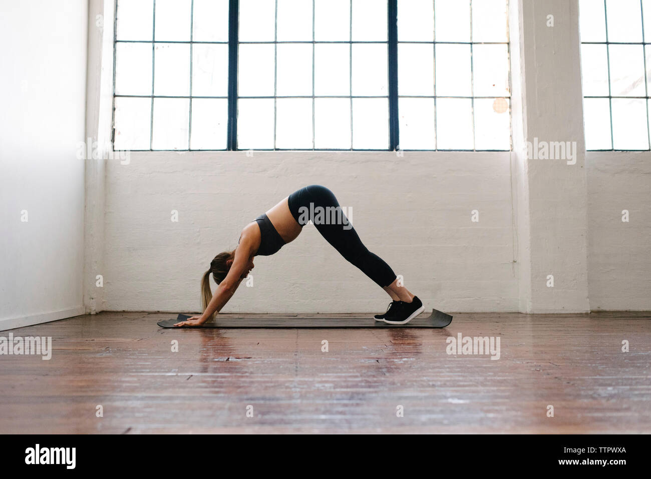 Side view of female athlete practicing downward facing dog position in gym Stock Photo