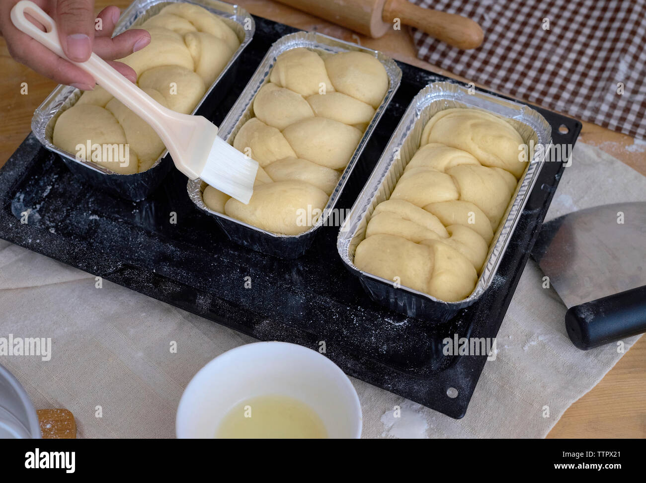 Cropped hand of baker applying egg white with brush on bread in container Stock Photo