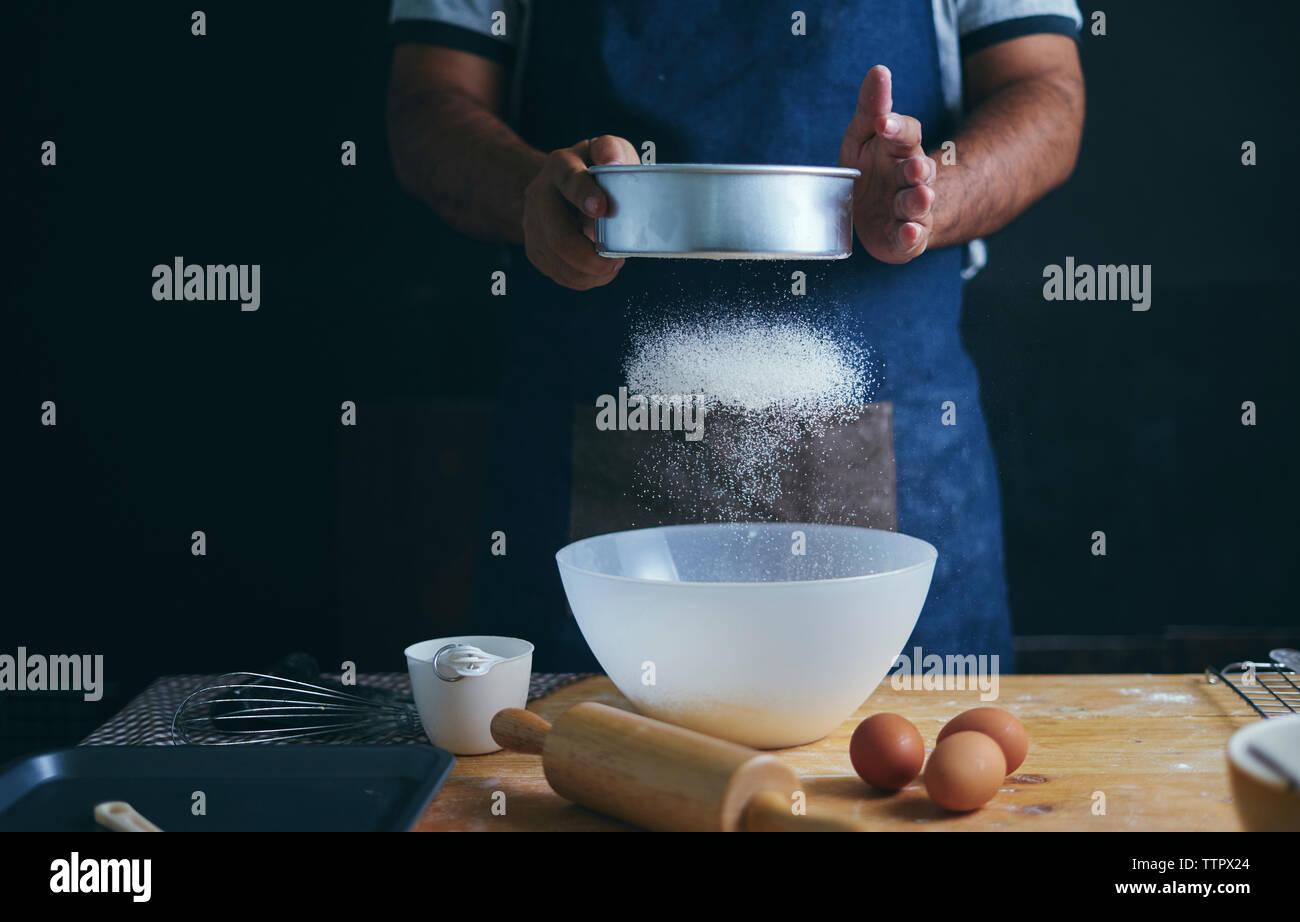 Midsection of man preparing food while standing in bakery Stock Photo