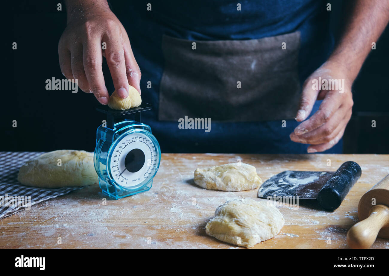 Midsection of man weighing dough while preparing food at table in bakery Stock Photo