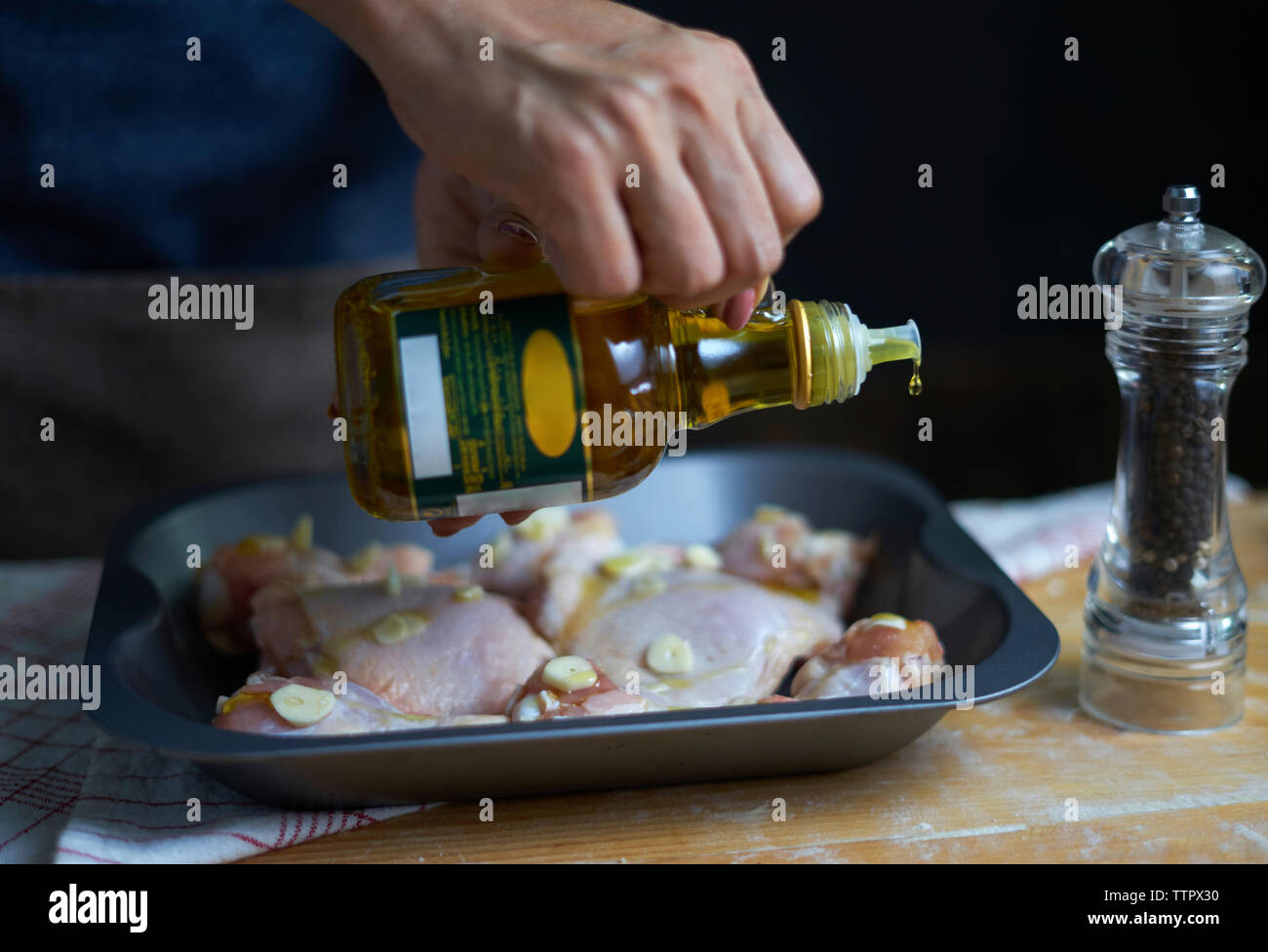 Midsection of woman pouring olive oil on chicken meat in tray Stock Photo