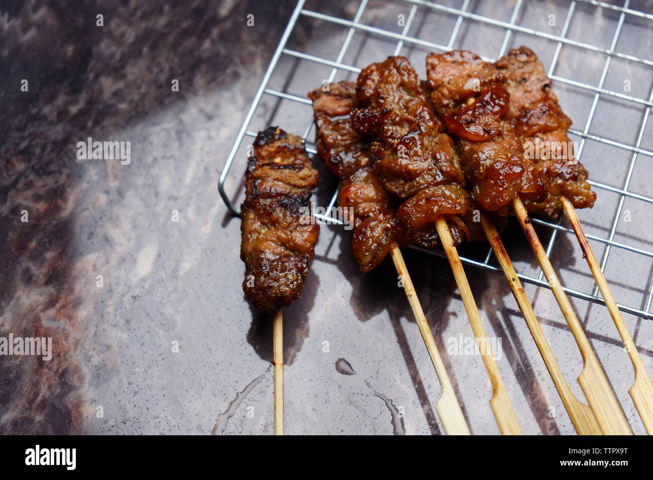 High angle view of grilled meats in skewers on metal grate over table Stock Photo