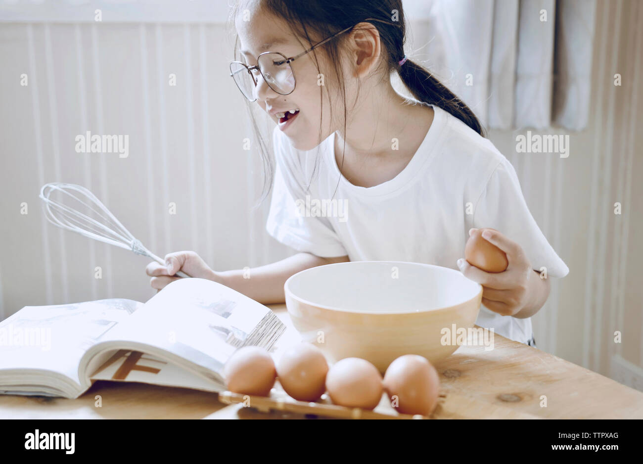 Smiling girl looking at cookbook while preparing food in kitchen Stock Photo