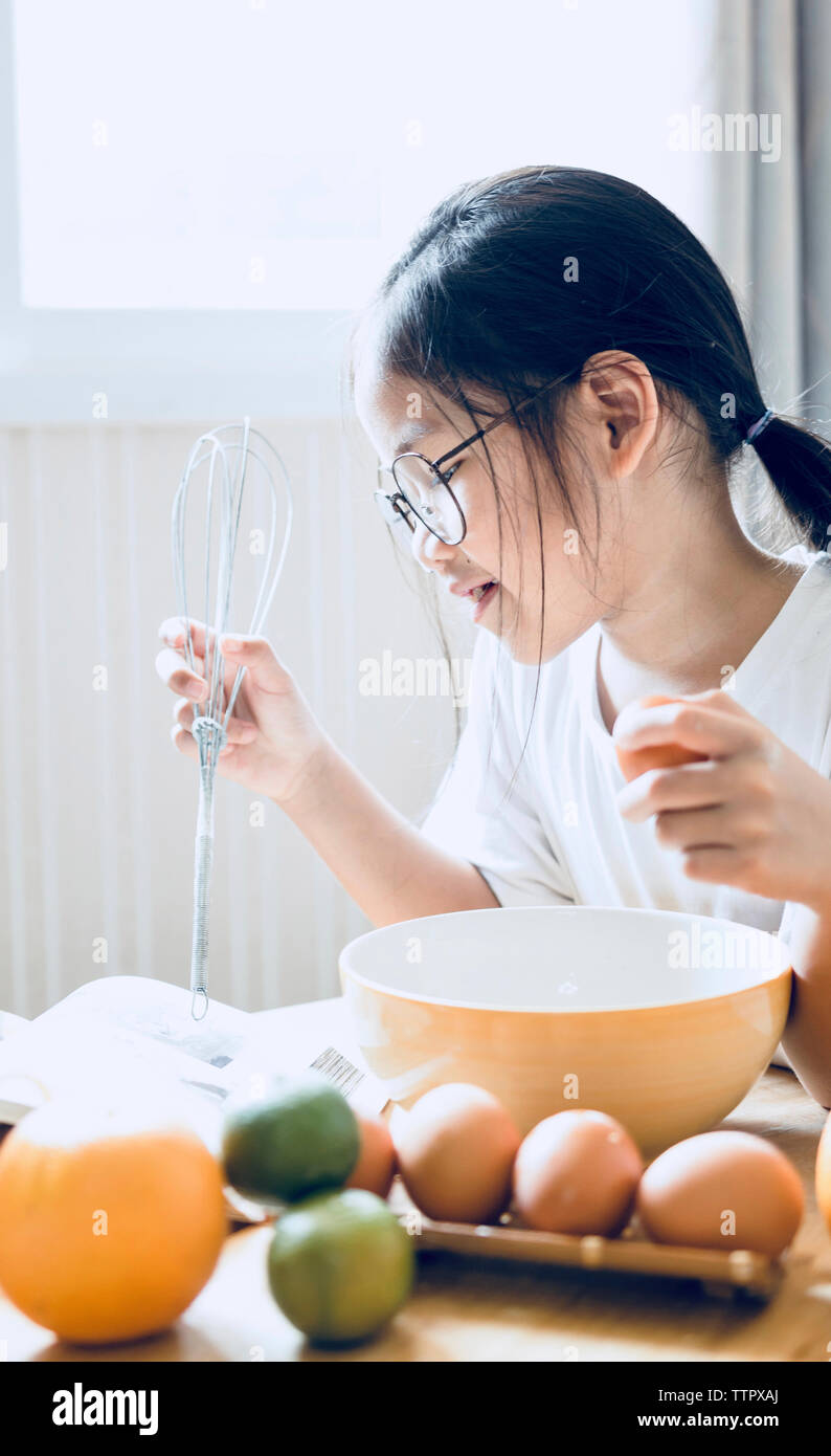 Girl reading cookbook while preparing food in kitchen at home Stock Photo