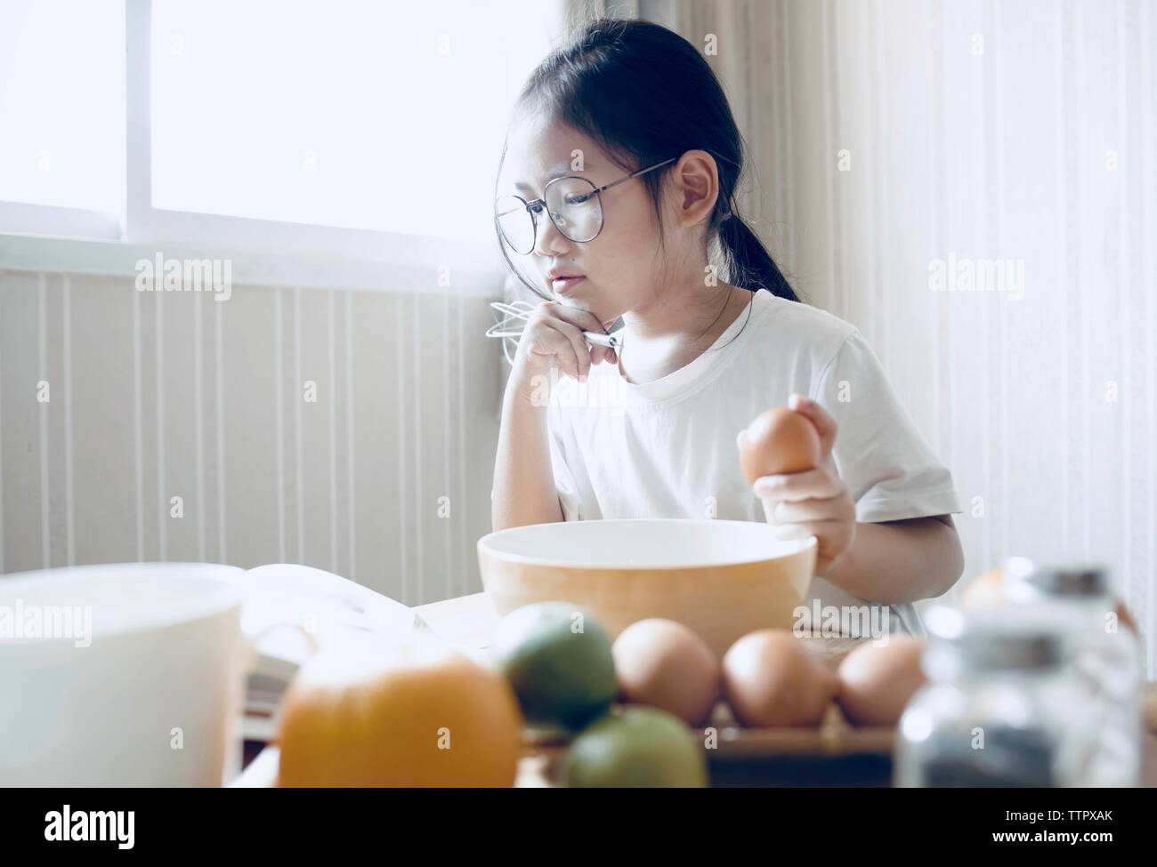 Girl reading cookbook while preparing food in kitchen Stock Photo