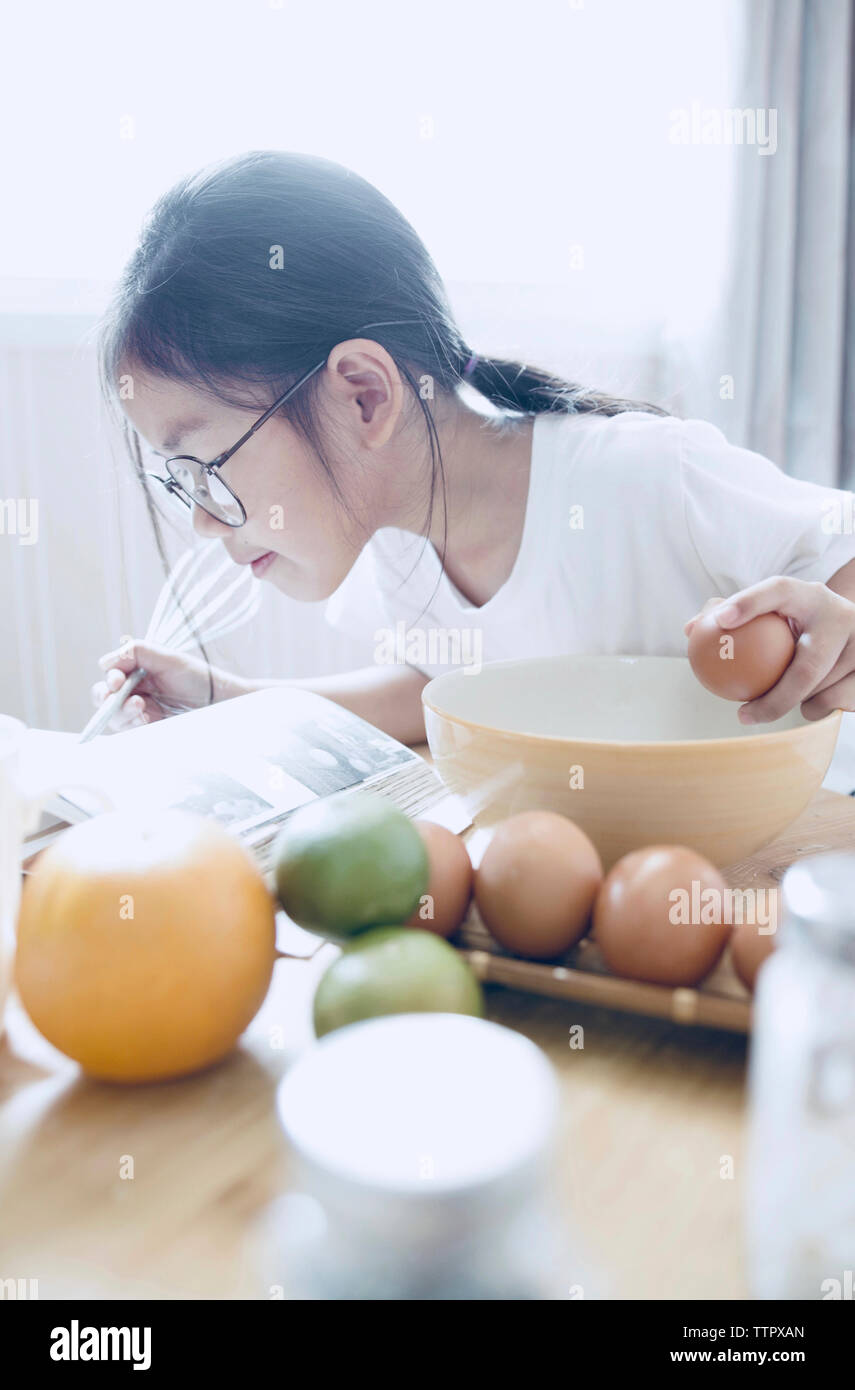 Girl reading cookbook while preparing food at home Stock Photo