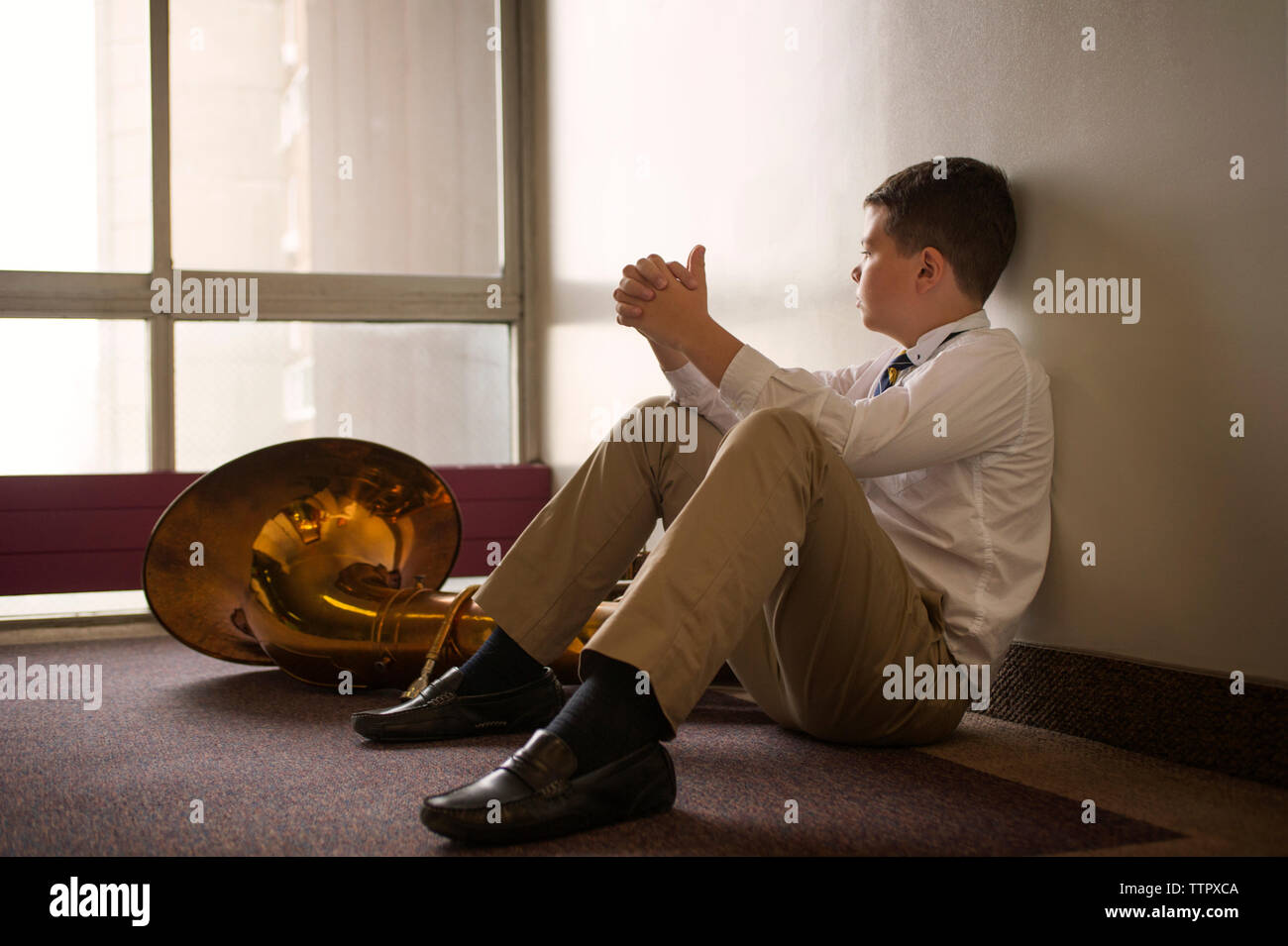 Thoughtful boy sitting by tuba on floor Stock Photo