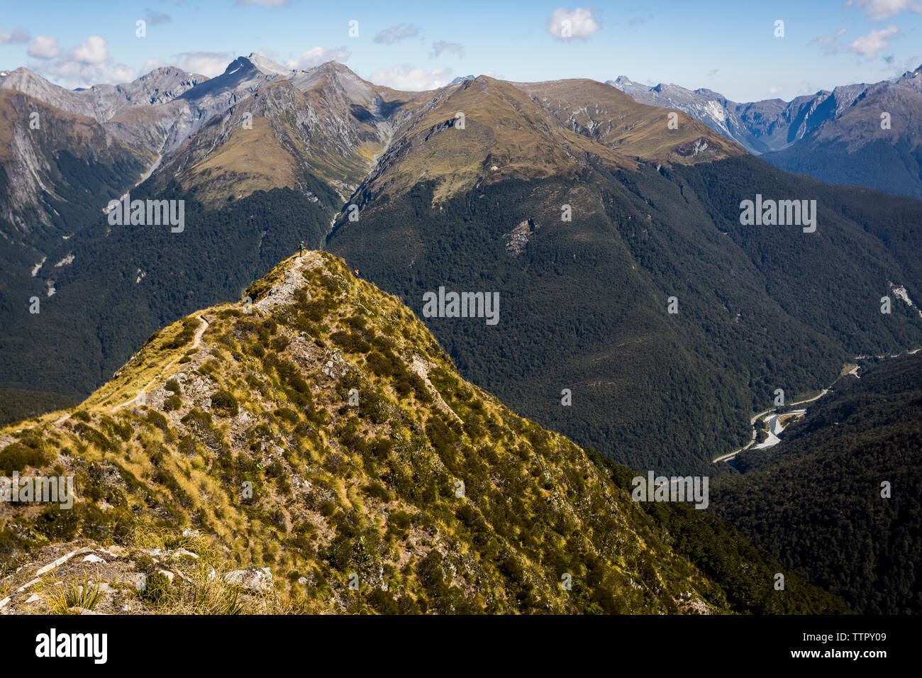 Figure on ridge trail overlooking mountains and valley in New Zealan ...