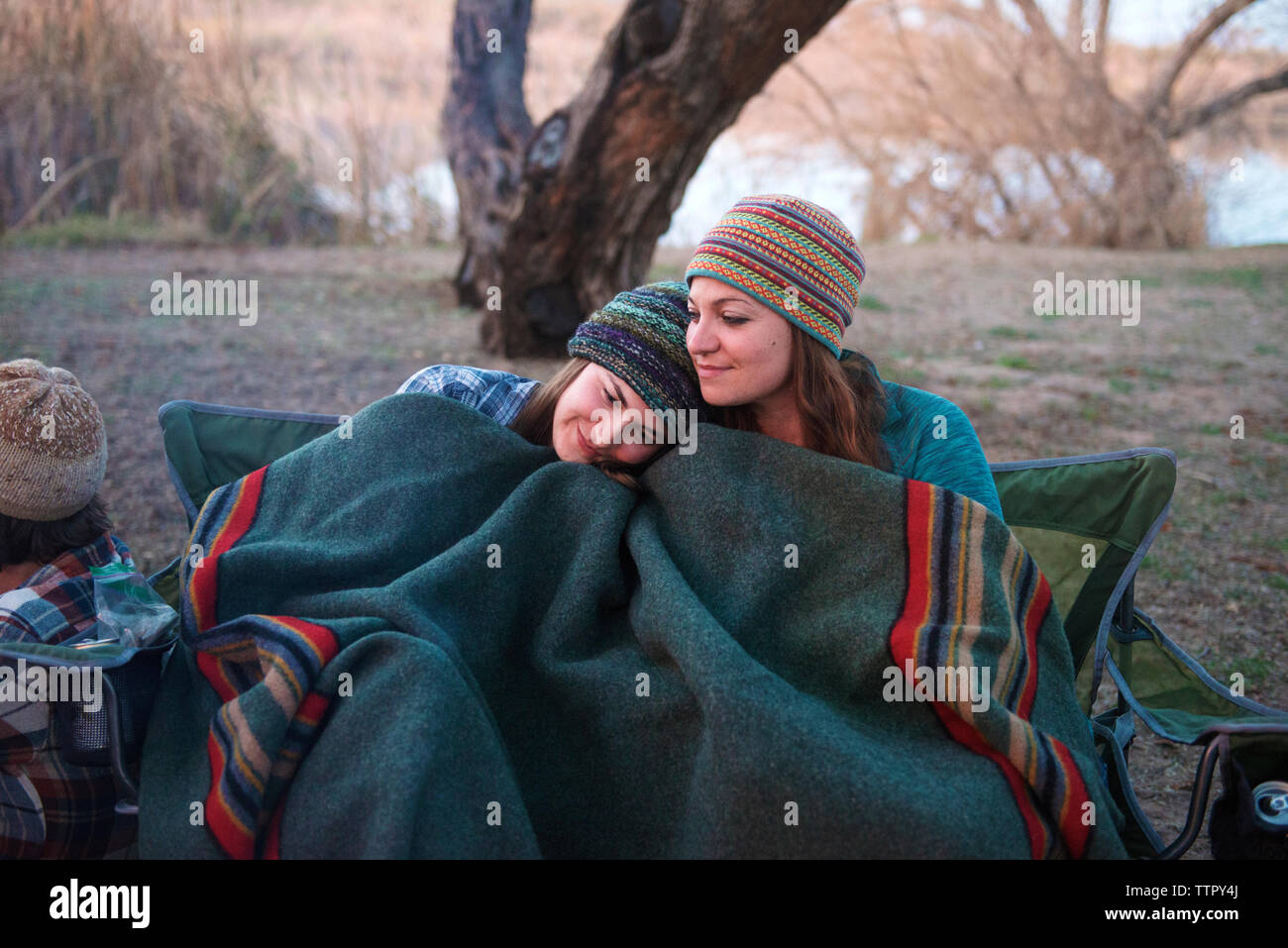 Affectionate female friends covered with blanket sitting at camp site Stock Photo