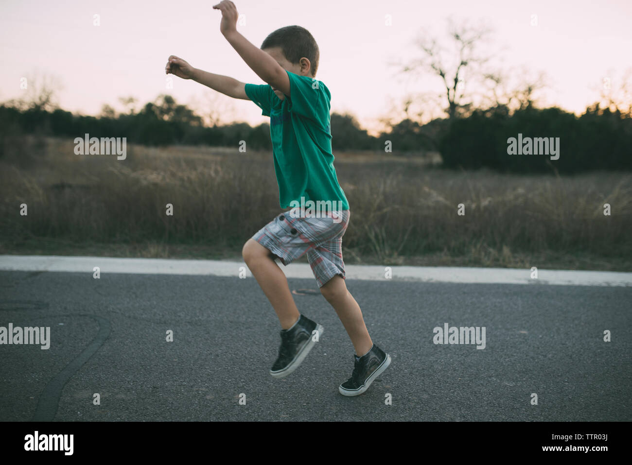 Side view of playful boy running on country road Stock Photo