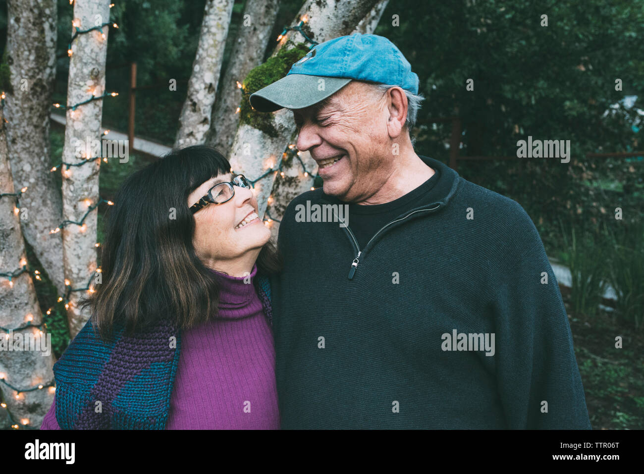 Happy senior couple looking face to face against decorated tree trunk at yard Stock Photo