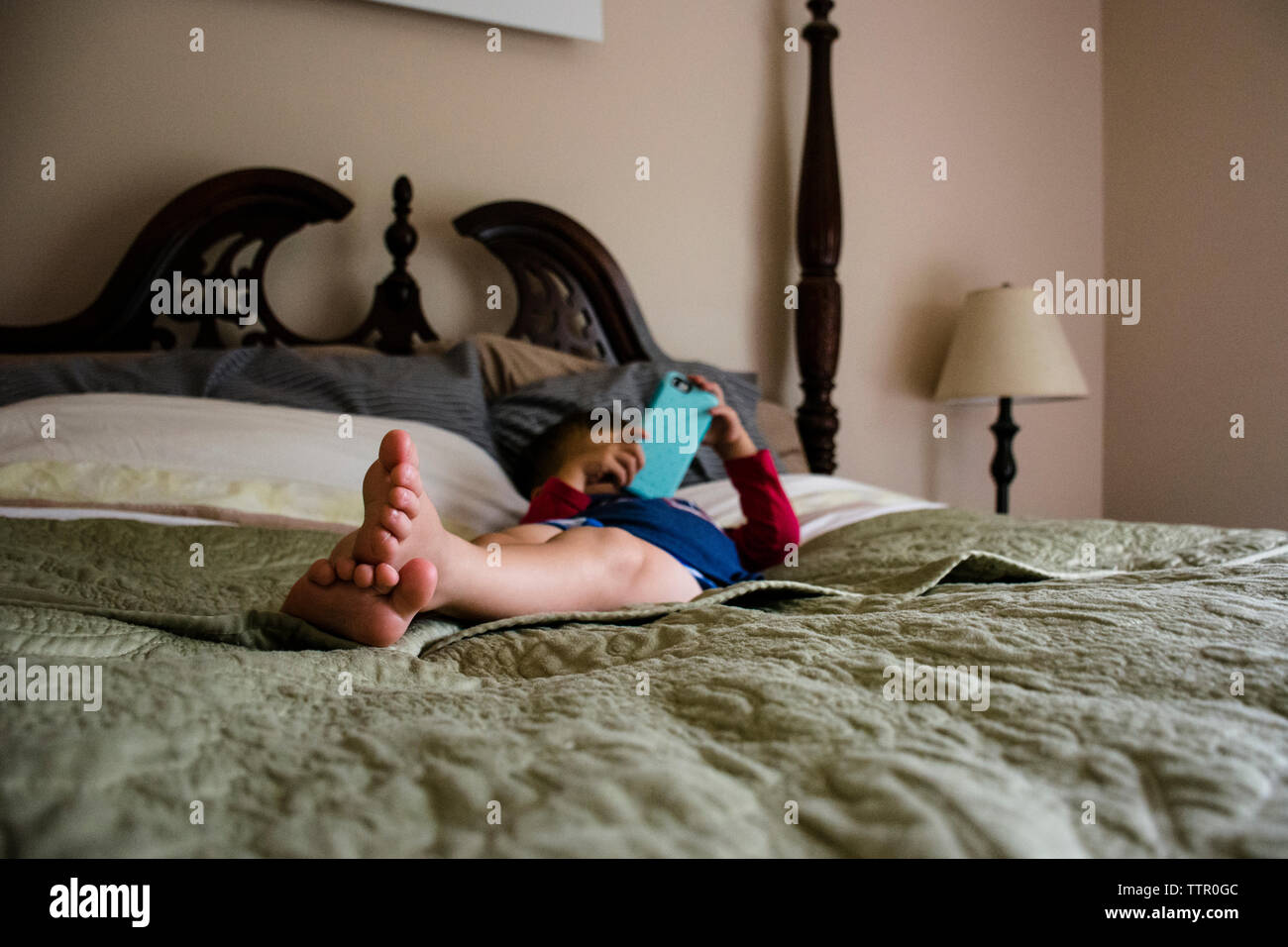 Boy using mobile phone while lying on bed at home Stock Photo