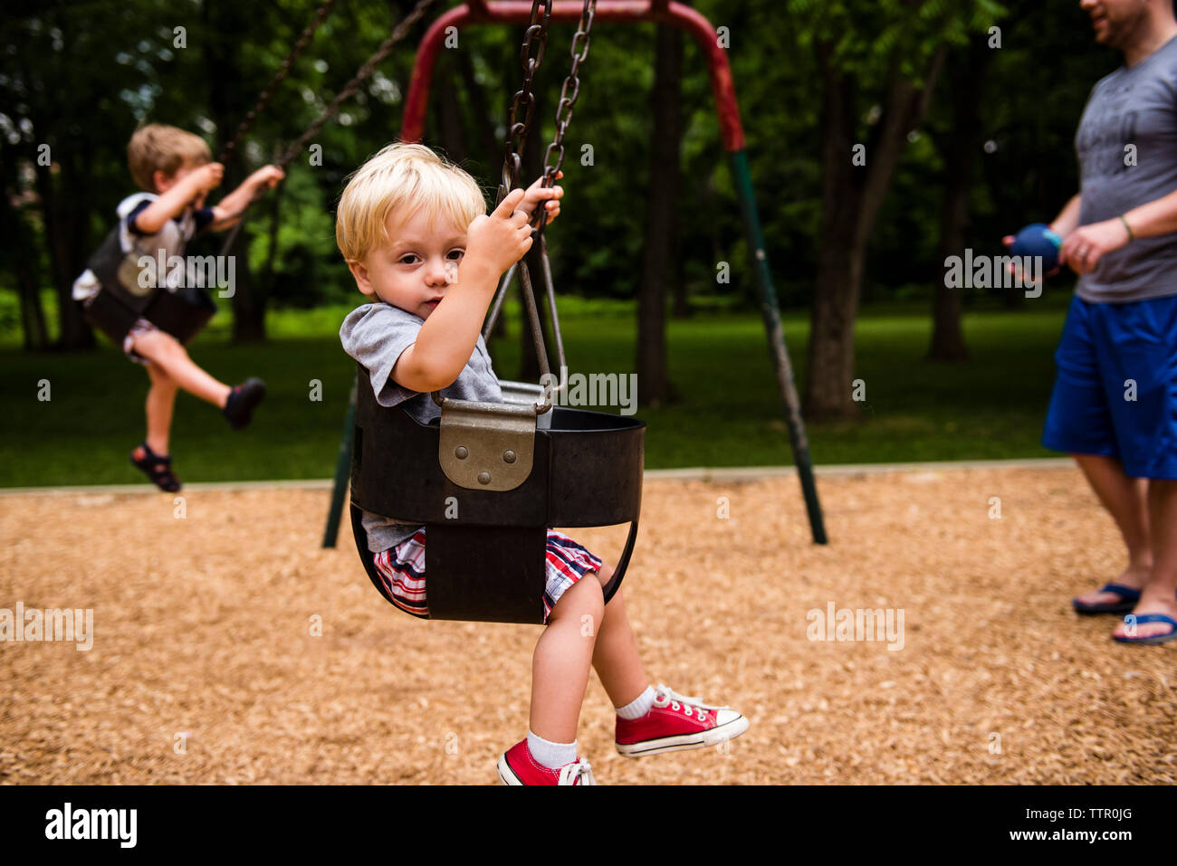 Low section of father with children enjoying swing in playground Stock Photo