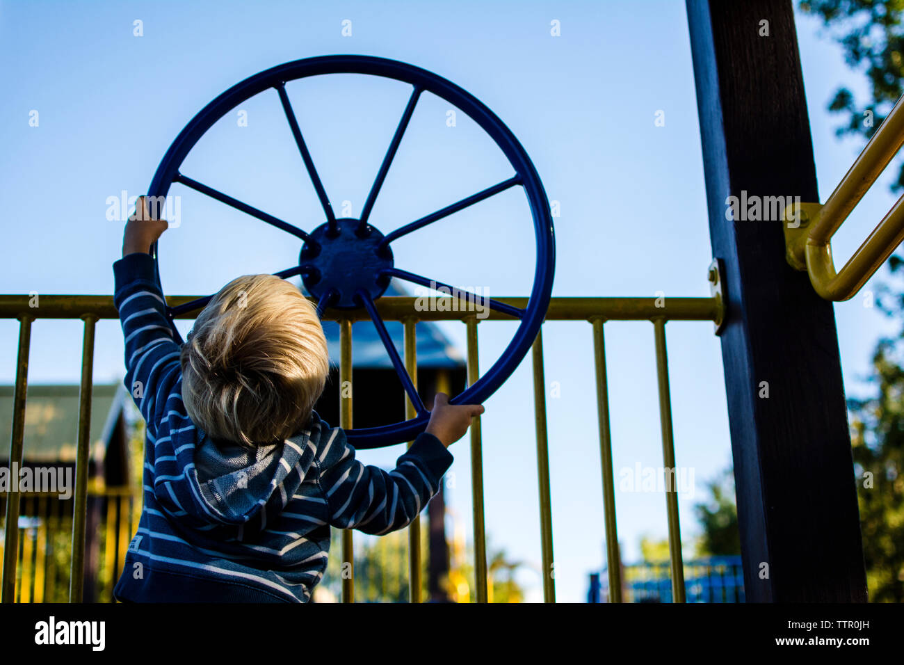 Rear view of boy spinning wheel on railing at playground Stock Photo