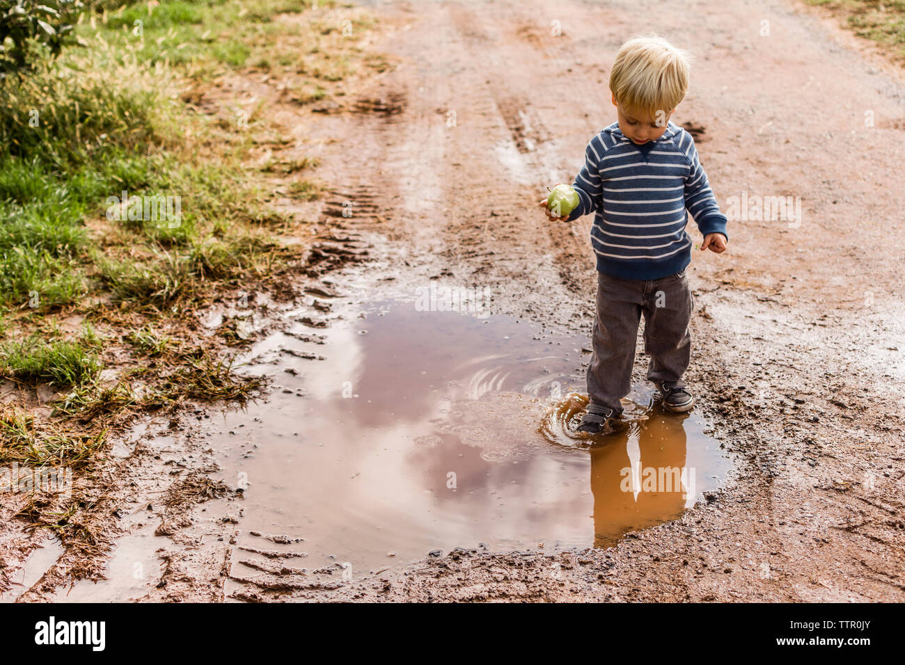 Boy with apple standing in dirty puddle Stock Photo