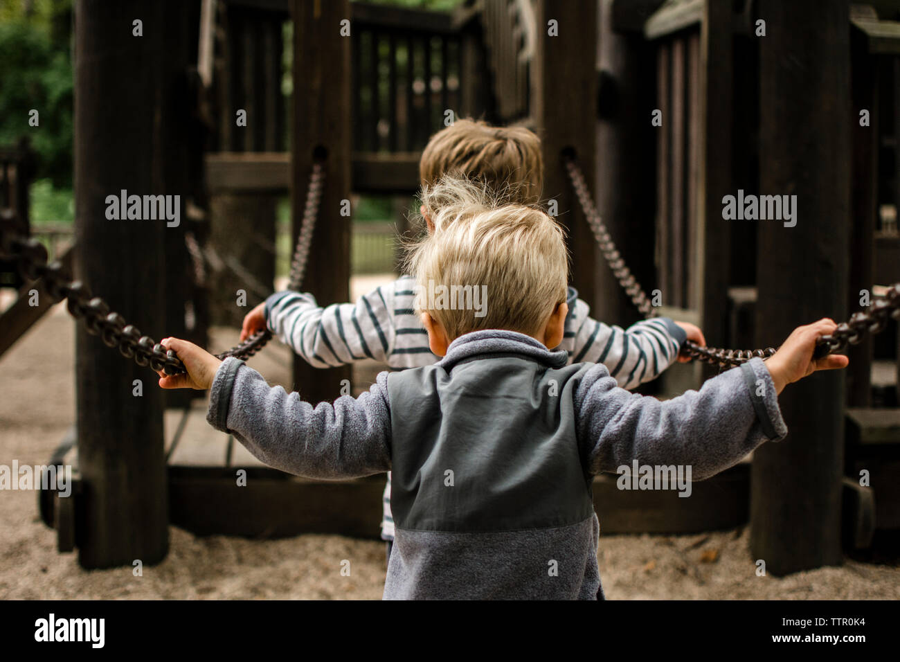 Rear view of brothers holding chain against jungle gym Stock Photo