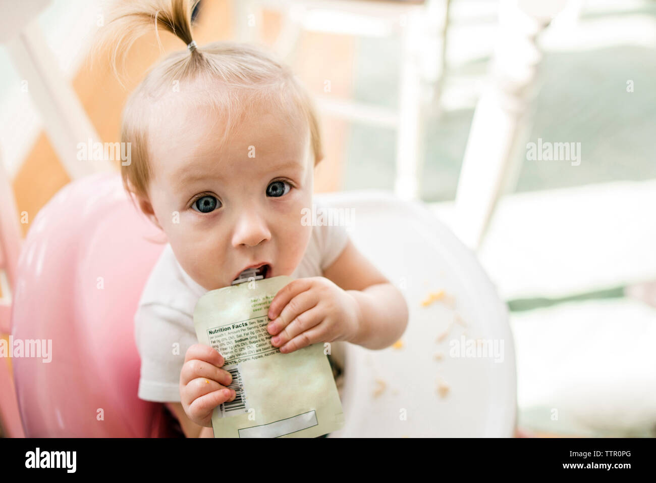 High angle portrait of cute baby girl eating apple sauce from pack