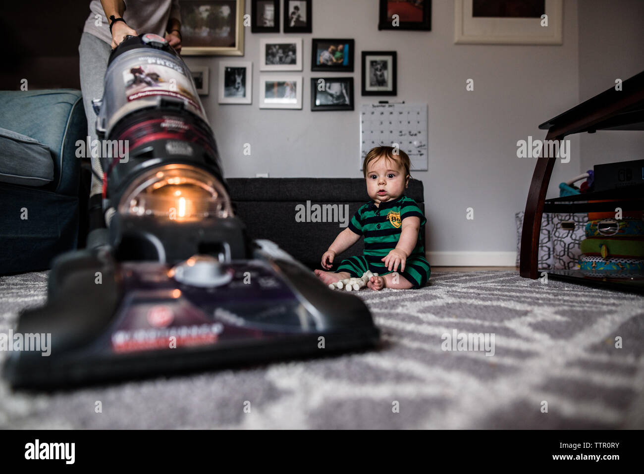 startled baby watches as mother vacuums the rug he is sitting on Stock Photo
