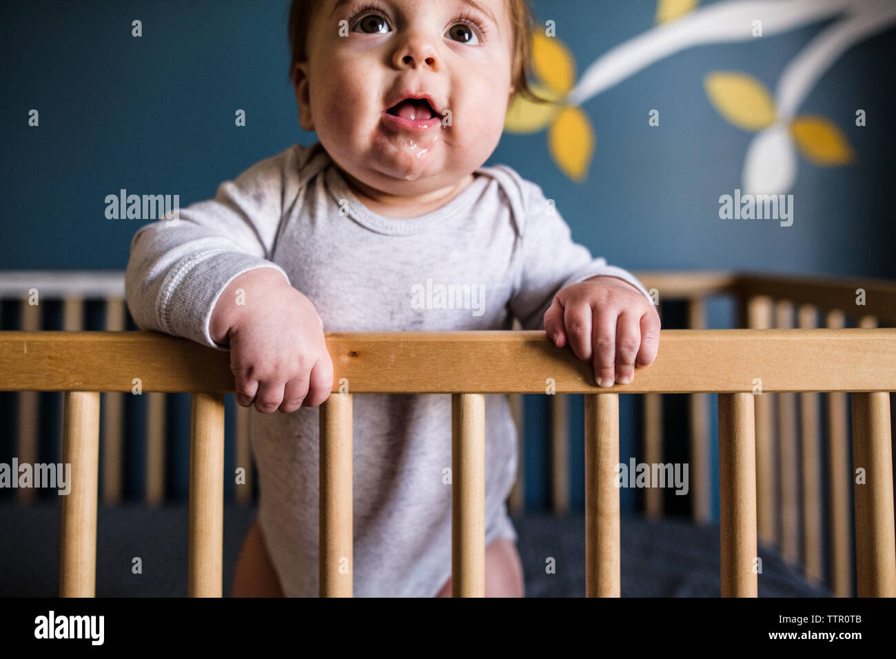 close up of drooling baby standing and leaning against crib rail Stock Photo
