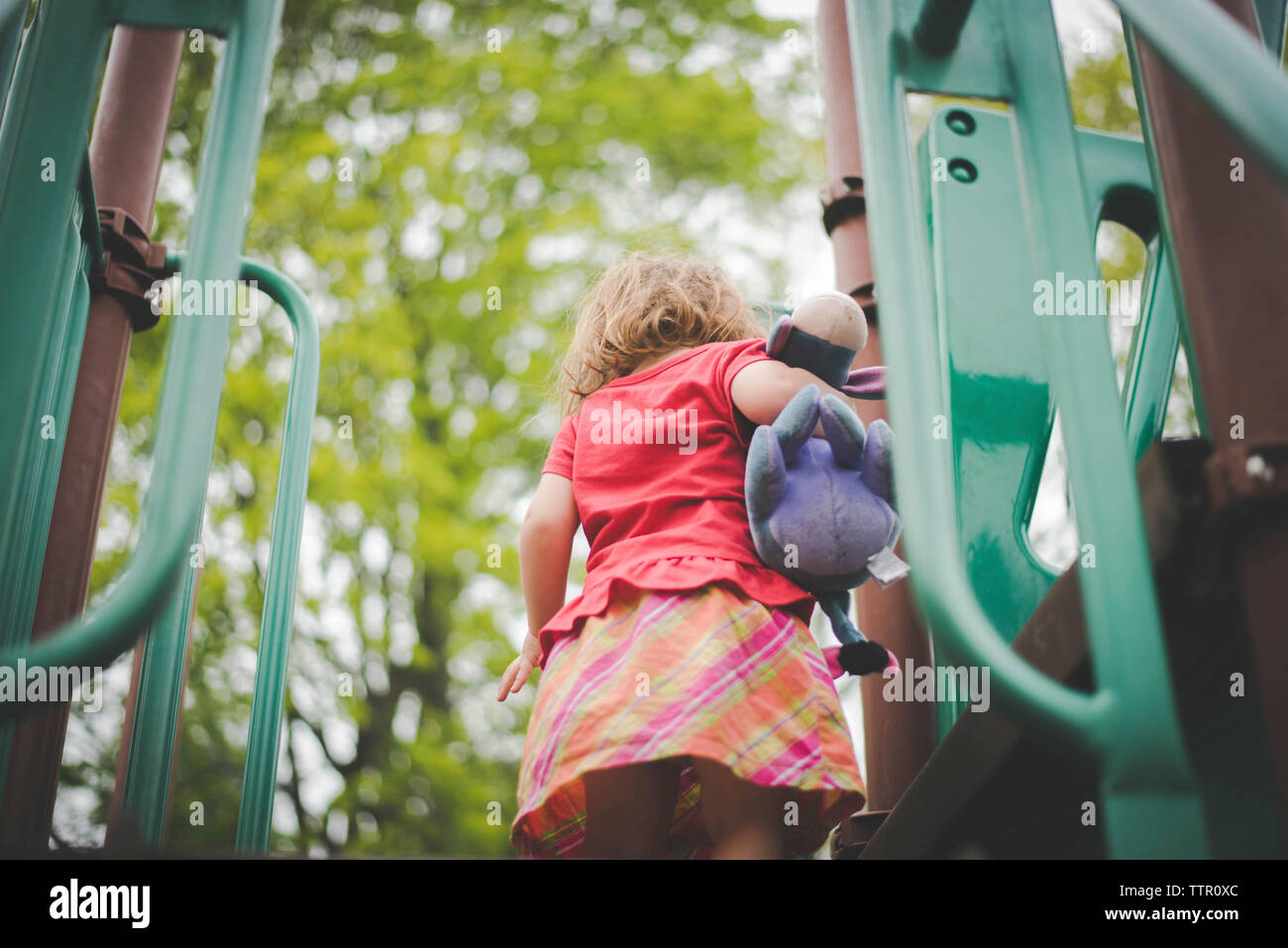 Low angle view of girl with stuffed toy standing on outdoor play equipment Stock Photo