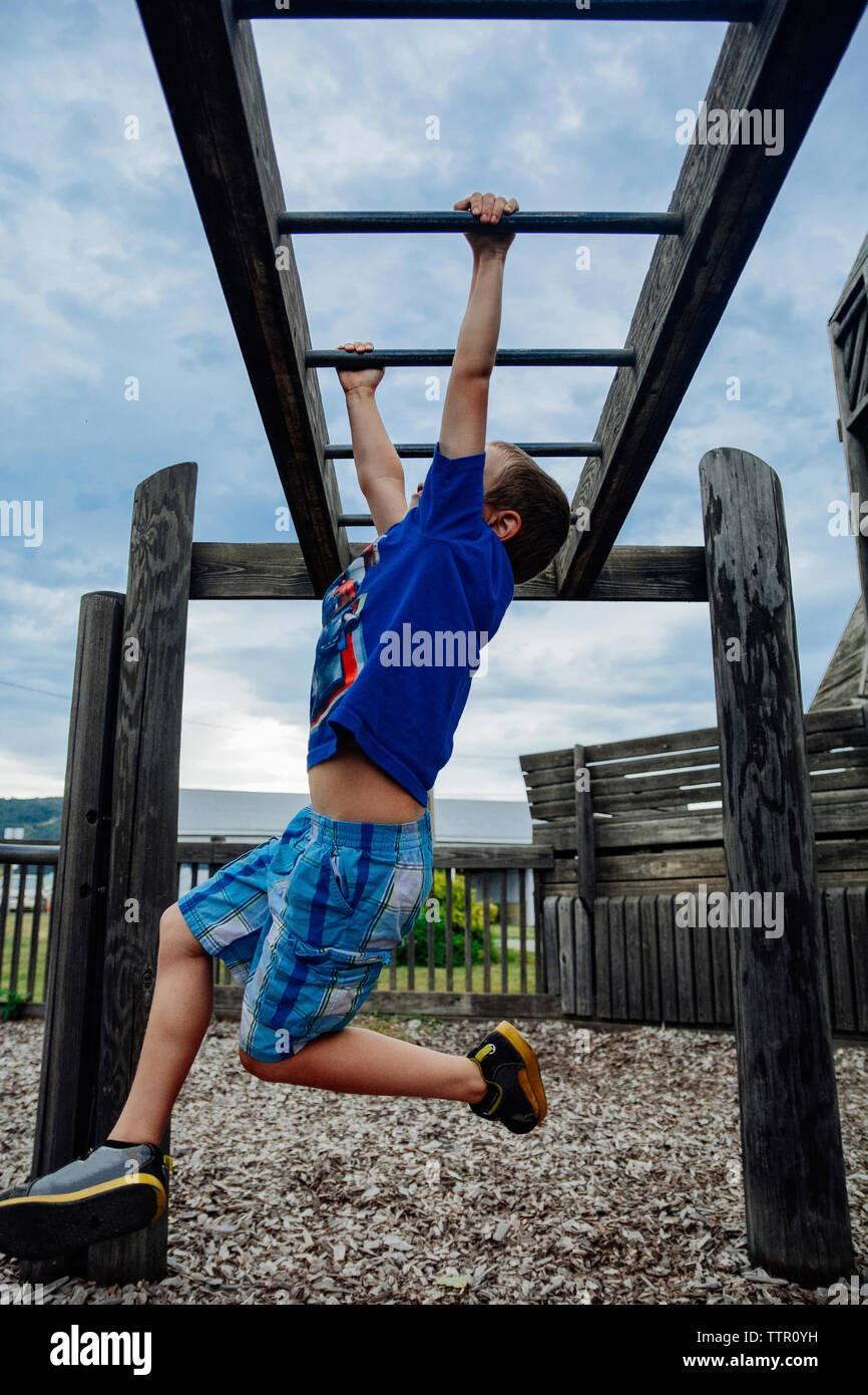 Boy hanging from monkey bars in playground against sky Stock Photo