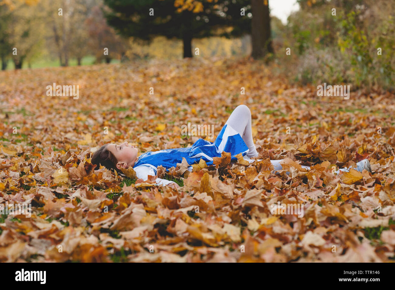Girl relaxing on field covered with autumn leaves in park Stock Photo