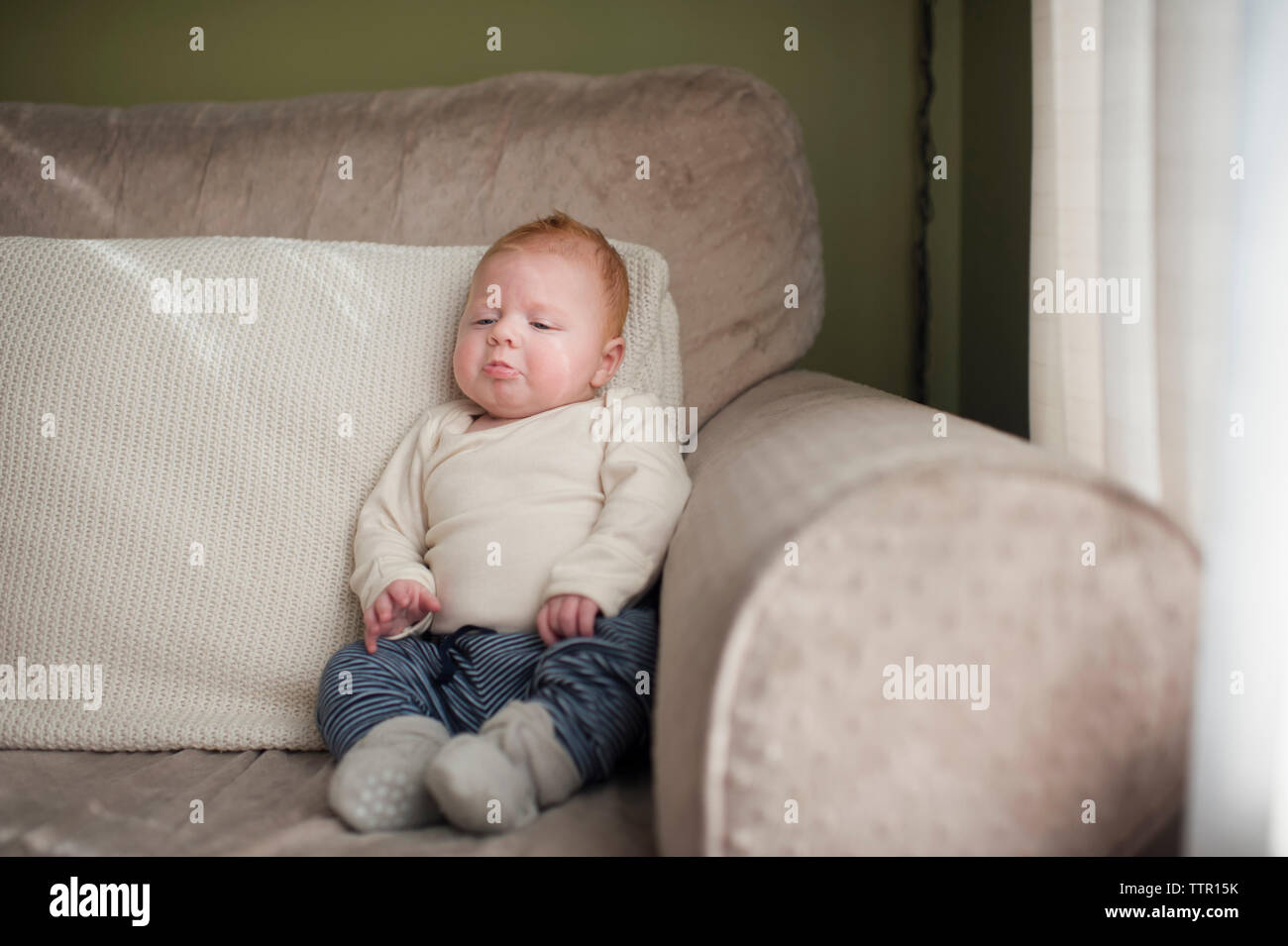Cute baby boy frowning while sitting on sofa at home Stock Photo