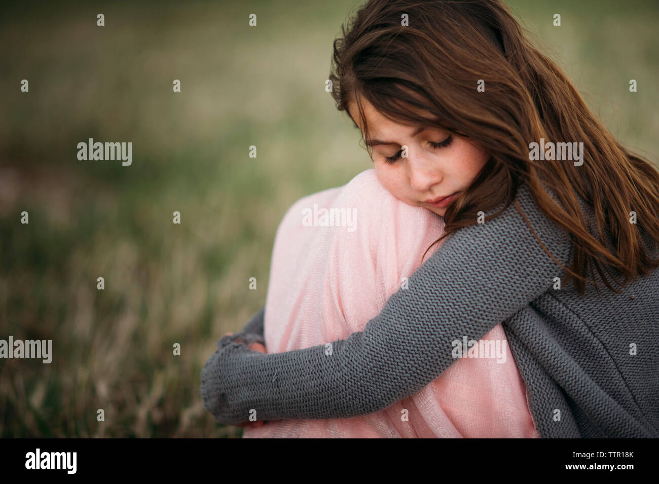 Girl with eyes closed hugging knees while sitting at park Stock Photo