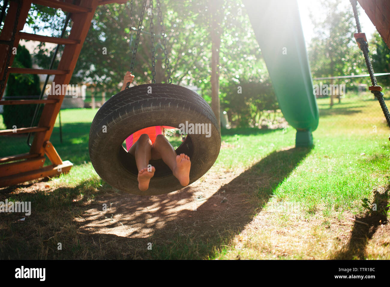 Low section of boy swinging in tire swing at playground Stock Photo