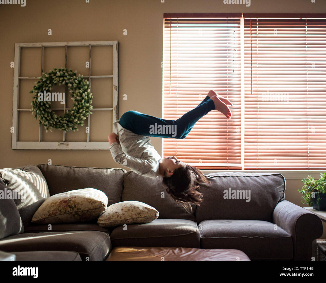 Full length of girl backflipping on couch at home Stock Photo