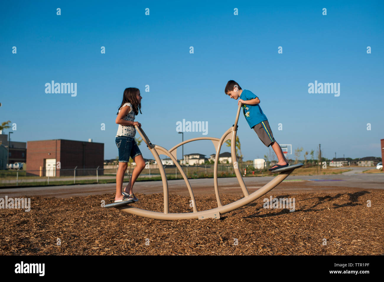 Side view of siblings playing on outdoor play equipment against clear blue sky at playground Stock Photo