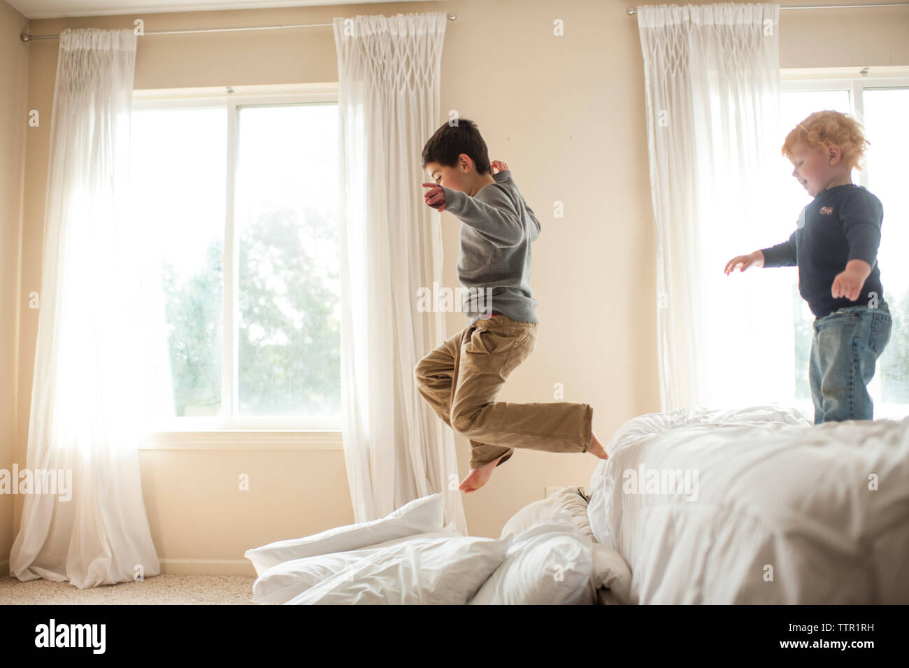 Brother having fun jumping off bed into pillows in bedroom Stock Photo
