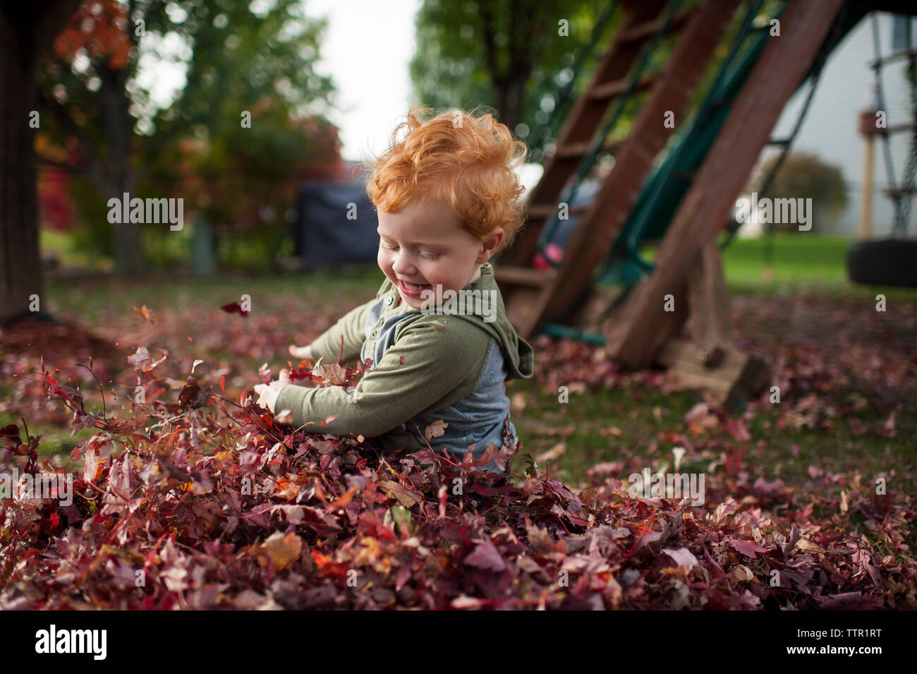 Sweet toddler boy smiles while playing in leaves in backyard Stock Photo
