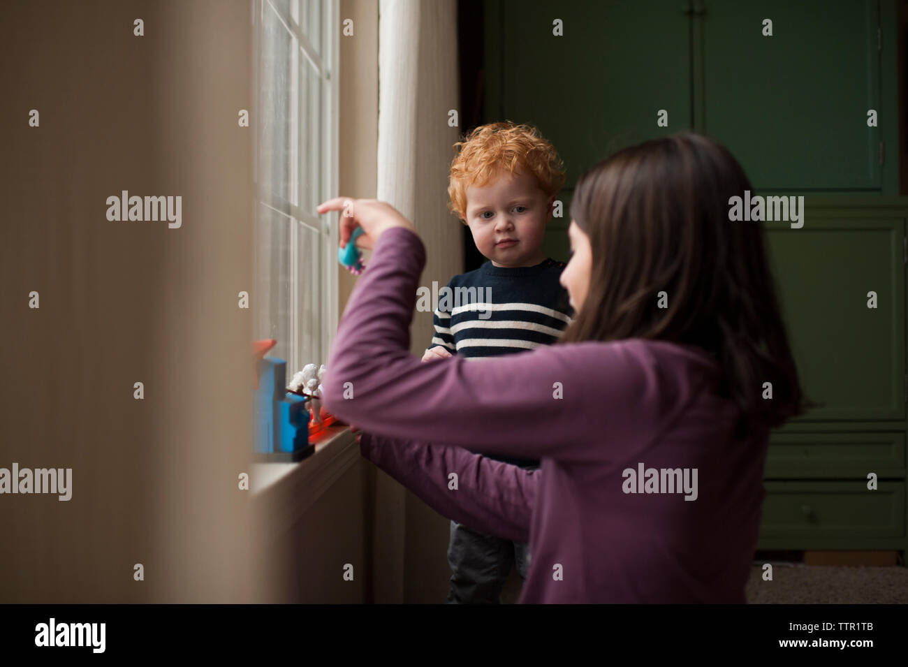 little brother watching big sister play with toys at home Stock Photo