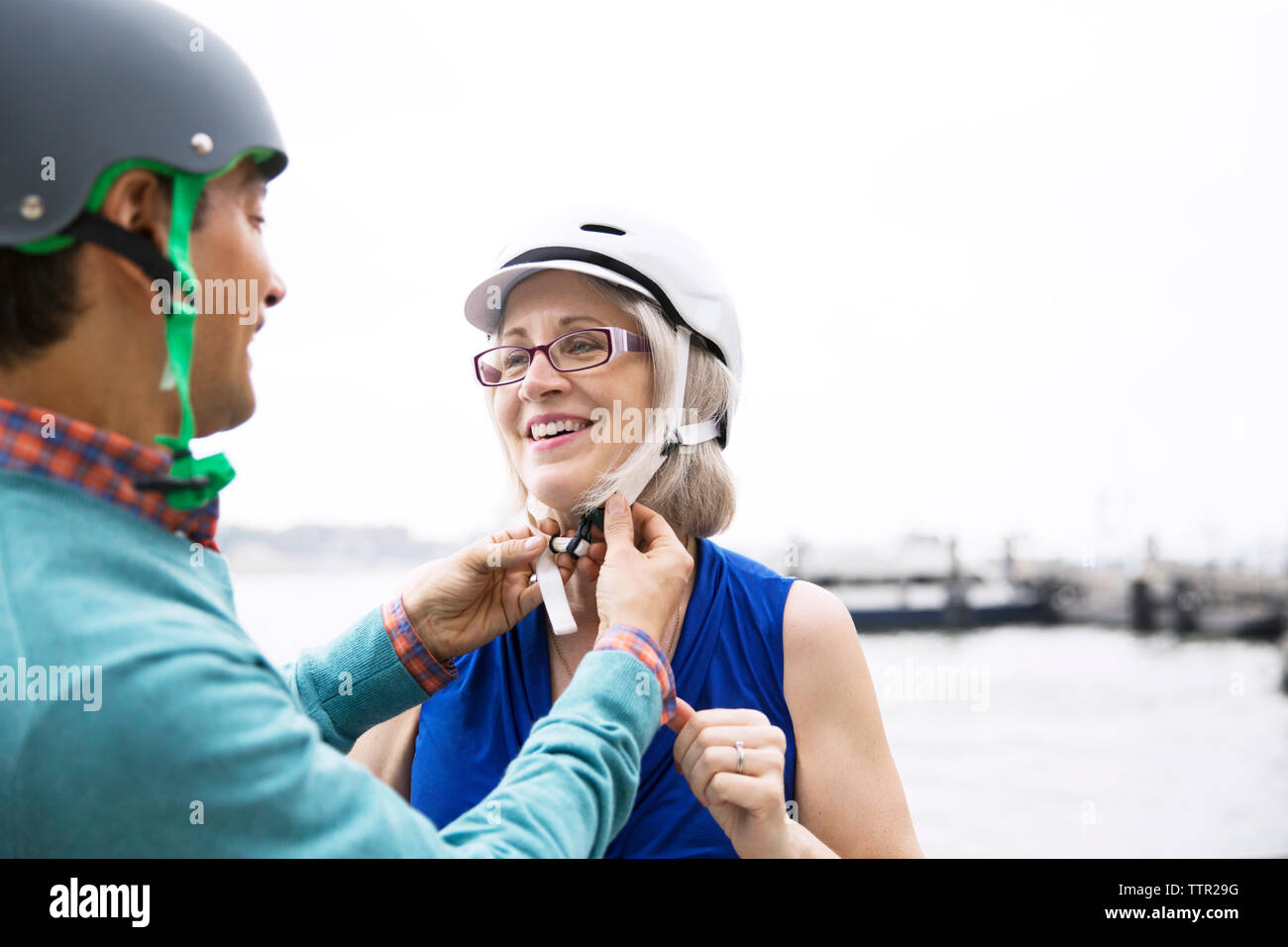 Mature man assisting woman in wearing bicycle helmet against clear sky Stock Photo