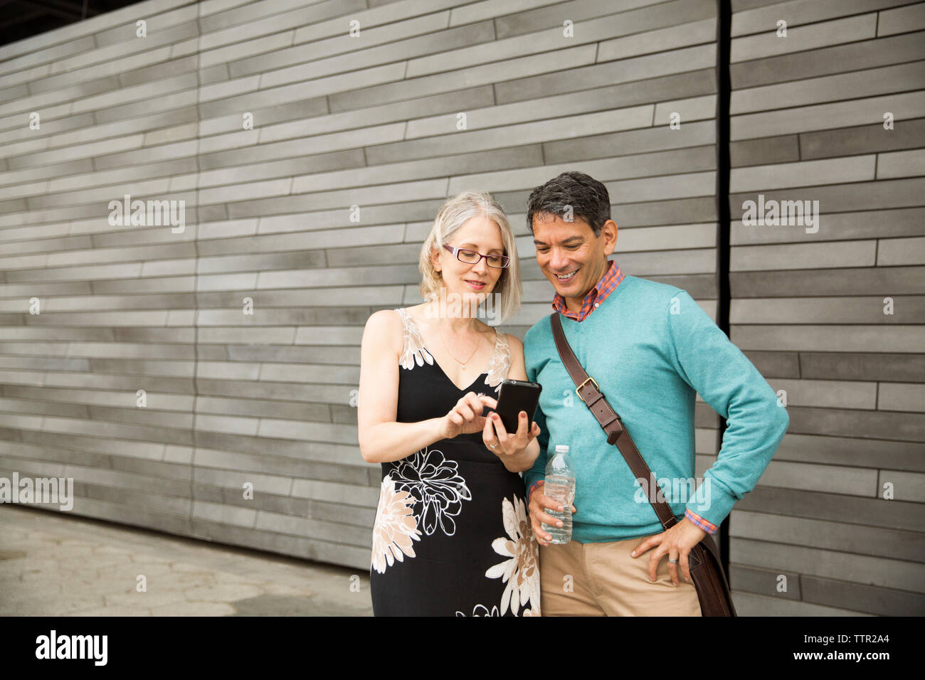 Mature couple using smart phone while standing against wall Stock Photo