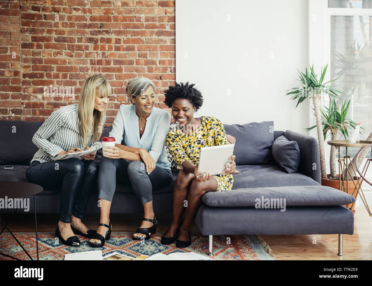 Happy businesswomen using tablet computer while sitting on sofa in creative office Stock Photo