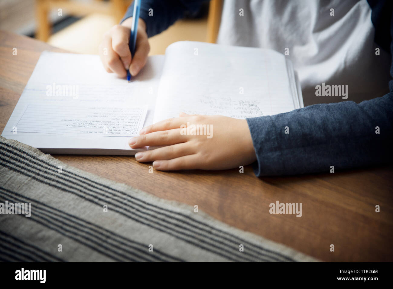 Midsection of boy writing in book on table at home Stock Photo