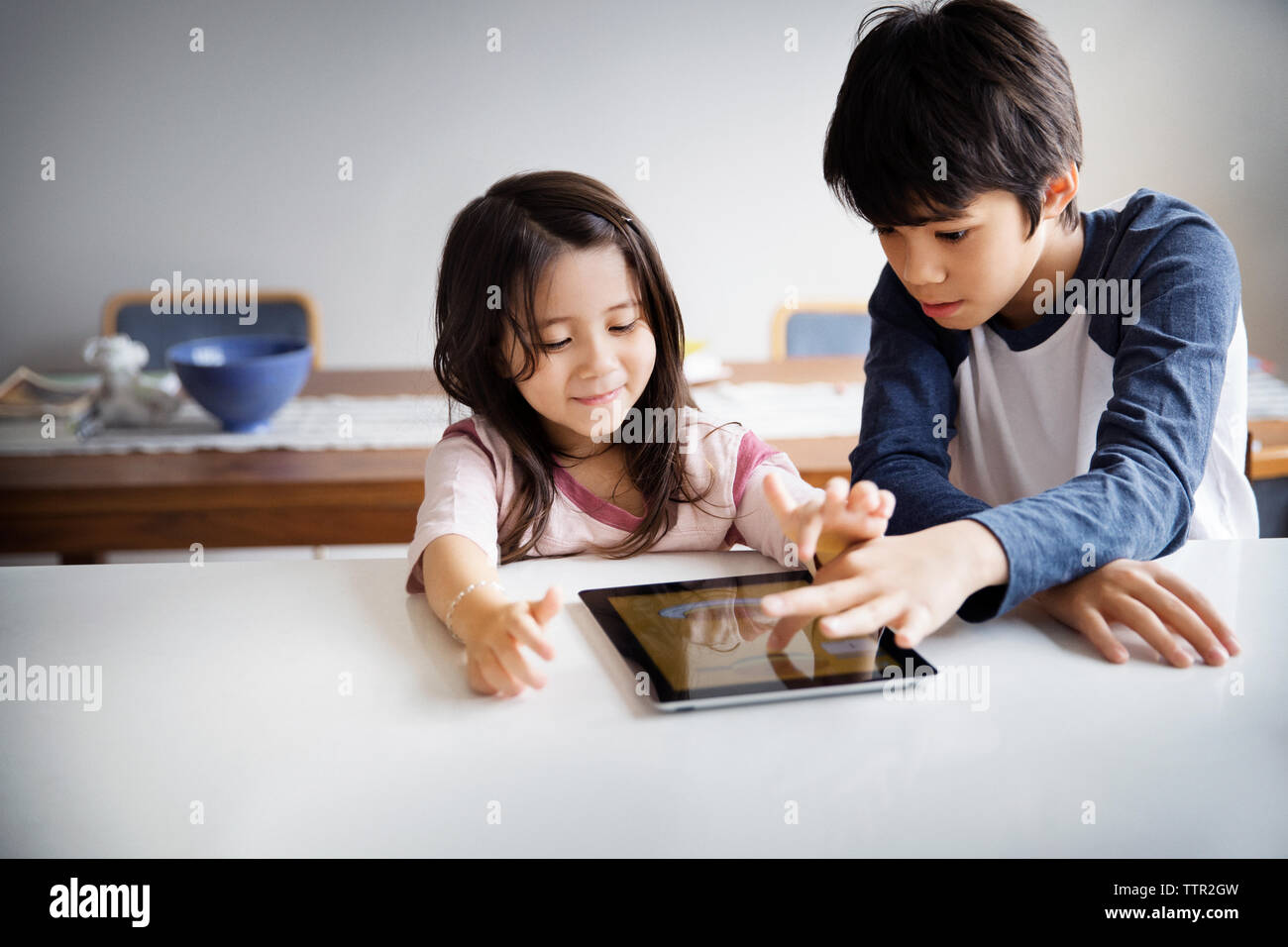 Siblings using digital tablet on table at home Stock Photo