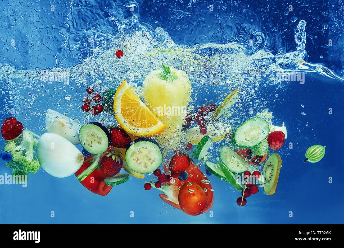Vegetables and fruits falling into water on color background Stock