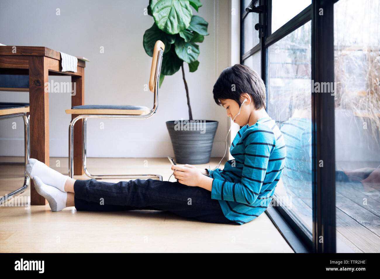 Boy using digital tablet while sitting by window Stock Photo