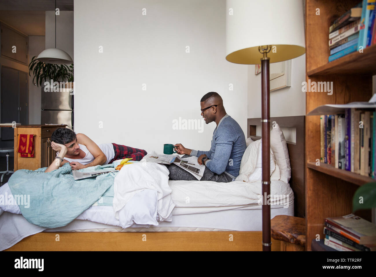 Gay men talking while reading newspaper in bedroom Stock Photo