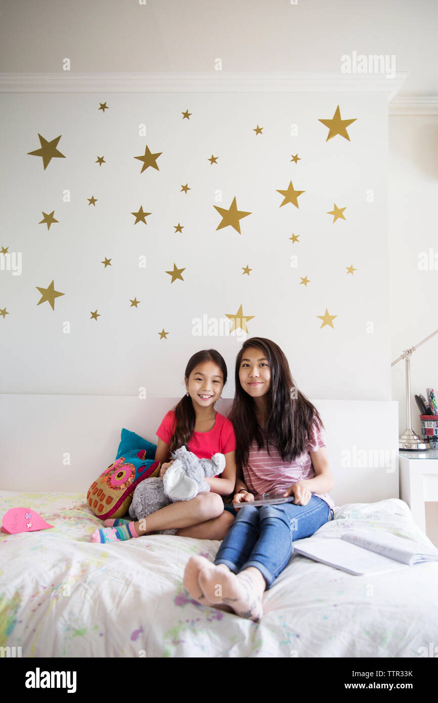 Portrait of smiling sisters sitting on bed at home Stock Photo - Alamy