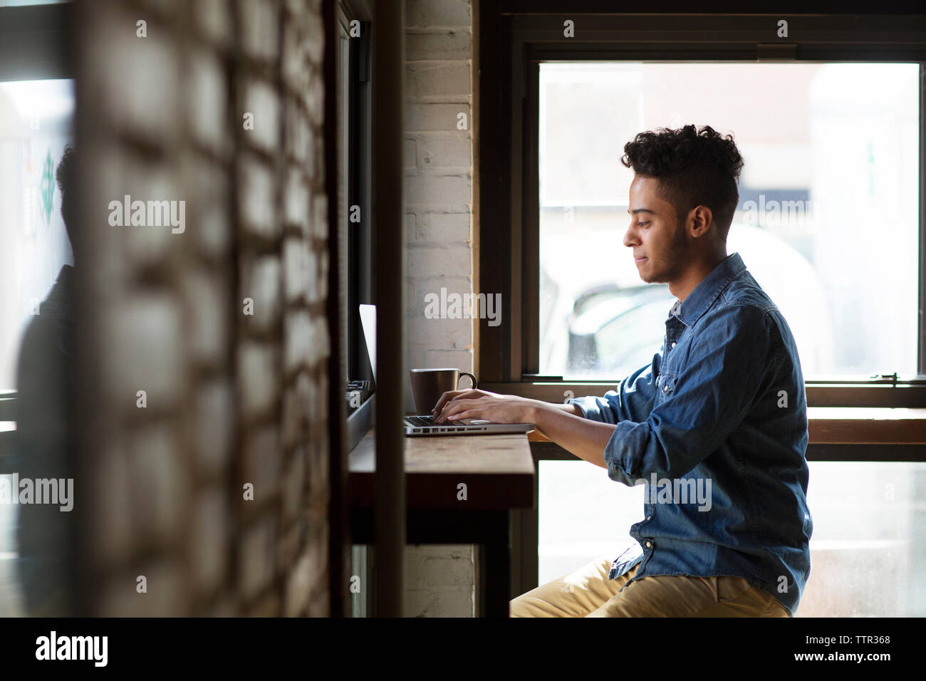 Side view of man using laptop while sitting by windows at cafe Stock ...