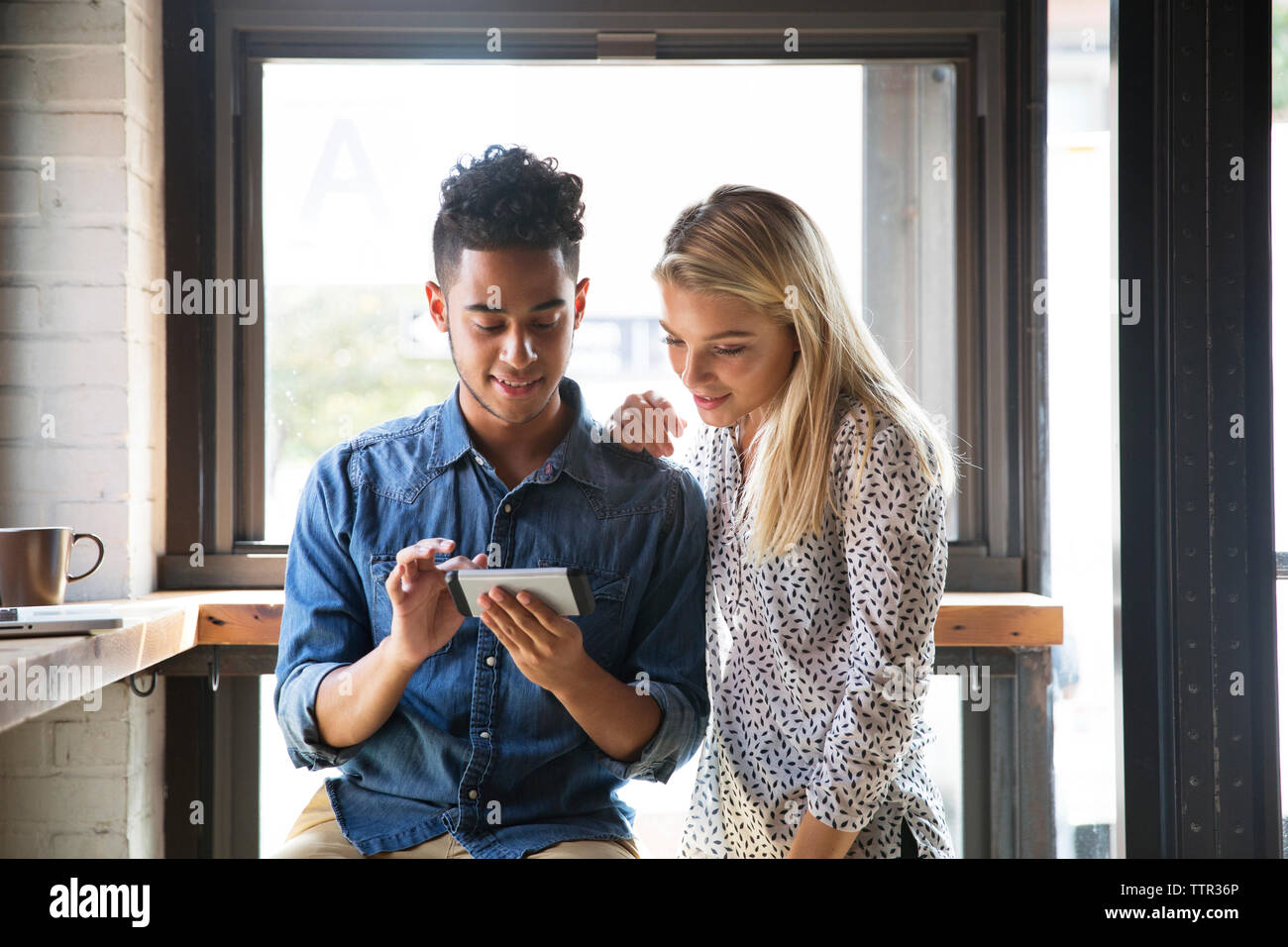 Smiling couple using mobile phone while sitting by window at cafe Stock Photo