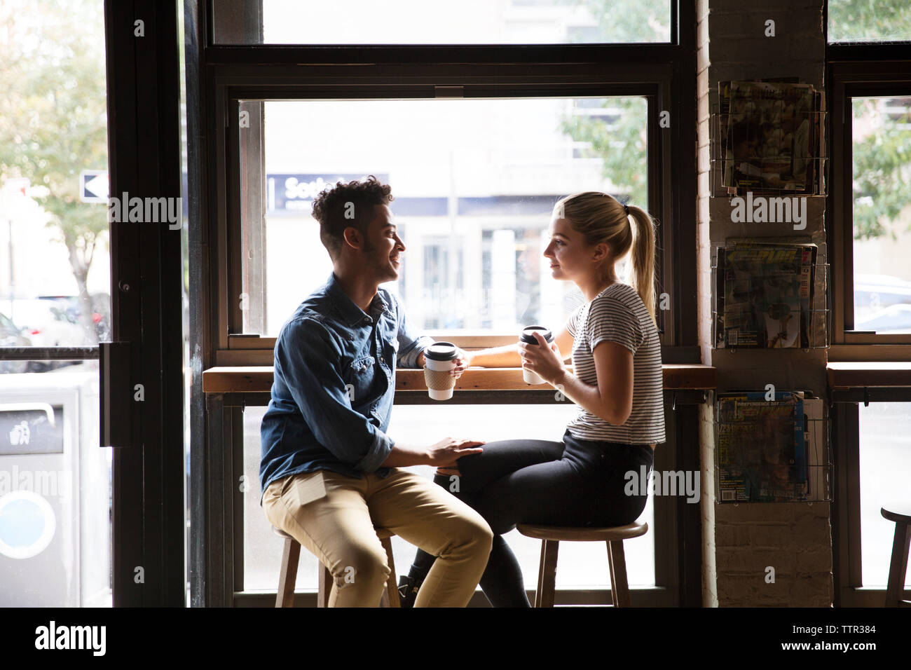 Smiling couple talking while sitting by window at cafe Stock Photo