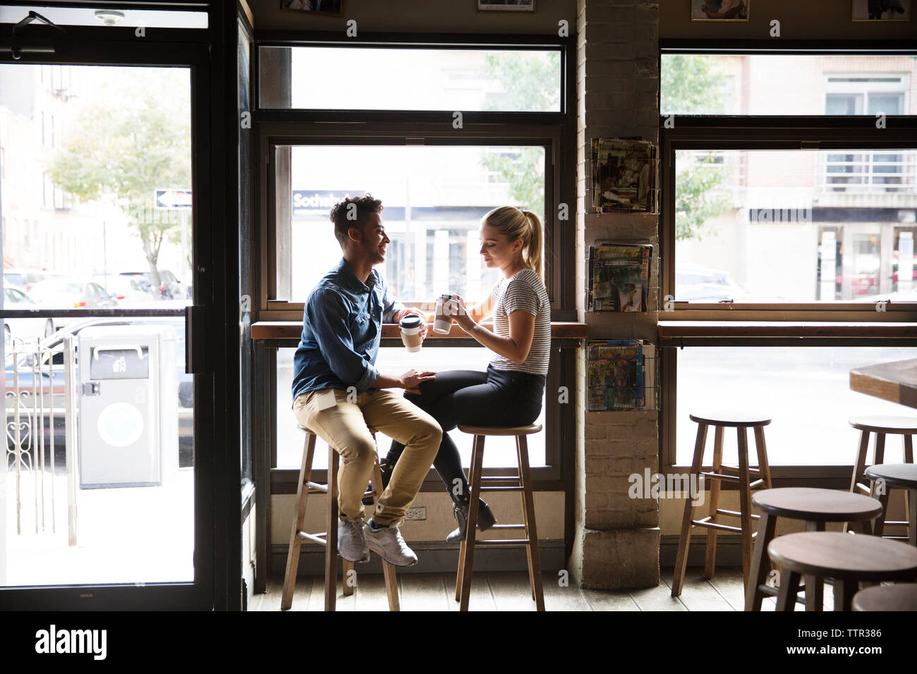 Smiling couple having coffee while talking by glass windows at cafe Stock Photo